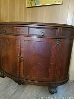 Front side view of 1920's mahogany French-Empire style rounded credenza showing ornate brass hardware, inlaid marquetry on drawer fronts, detailed beading, and carved claw feet.