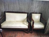 Pair of 1920s American-made mahogany French-Empire style settee and chair upholstered in cream fabric with nailhead trim, set against a curtain background.