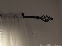 White sheer curtain panel hanging from a dark decorative rod with leaf motif finial, showing fabric texture and rod style