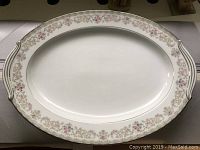 Top view of a white porcelain oval serving platter with floral border and handles