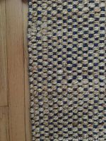 Close-up photo of the edge of the sisal runner showing tightly woven beige and dark blue fibers in a checkerboard pattern.