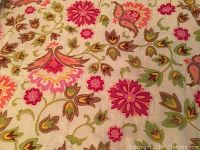 Close-up of the floral pattern side of the bedspread showing pink, green, brown flowers and leaves on a cream background.