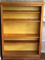 Front view of the handmade wooden bookcase showing four shelves and a yellow unfinished back panel.