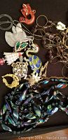 Photo of assorted costume jewelry including animal-themed pins, turtle charm, iridescent bead necklace, and multi-layered dark bead necklace.