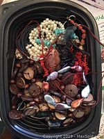 Overhead photo of a plastic container holding various bead jewelry including pearl-like, wooden, red coral-like, and iridescent teardrop beads