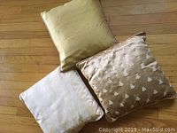 Three silk-covered throw pillows arranged on hardwood floor, showing front sides with varied texture and pattern.