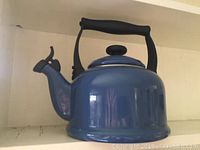 Side view of the blue Le Creuset tea kettle showing its shape, spout, handle, and lid.