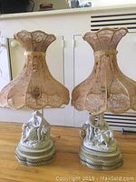 Pair of Meissen-style lamps showing porcelain figurine bases with lace fabric shades.