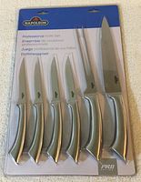 Full view of the 6-piece knife set sealed in original packaging, shows all knives and carving fork with stainless steel handles and blades.