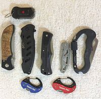 Top view of nine mixed pocket knives placed on a light background showing variety in size, handle materials and colors
