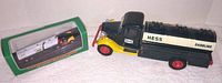 Large Hess gasoline truck bank with black and cream body, red wheels, yellow accents, and working lights shown on white surface.