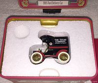 Top-down photo showing the 1905 Ford Delivery Van miniature replica inside white foam packaging within the original tin box. The van is black with branded Texaco and Texas Company logos.