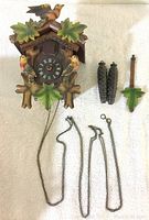 Front view of cuckoo clock with carved birds and leaves, weights, pendulum and chains laid beside it
