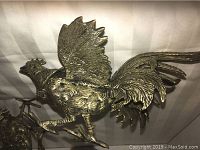 Close-up view of one silvertone fighting cock figurine showing detailed feathers and pose.