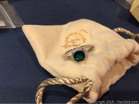 Ring displayed on Lenox branded cream drawstring pouch, front angle showing green stone and silver setting.