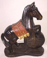 Front and side view of wooden horse figure showing horse rearing with saddle and base with carved details.