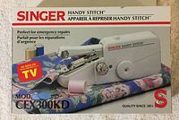 Photo of the Singer Handy Stitch model CFX300KD packaging box showing the sewing machine and fabric, highlighting it as perfect for emergency repairs.