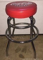 Full view of the red Coca-Cola bar stool showing the padded seat and chrome metal legs.