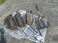 Four wire deep fryer baskets laid out on a tarp outside, showing the metal handles and construction of each basket.