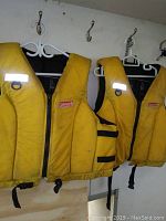 Three yellow Coleman life jackets hanging on hangers, showing front with zippers and Coleman logo patches visible.