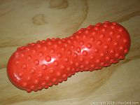 Red plastic back roller with raised bumps for muscle massage and stretching shown on wooden surface.