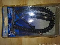 Photo of the 12 V coiled extension cord in original clear plastic packaging showcasing the coiled black cord and plug for power port use.