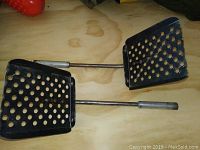Two heavy duty deep fryer utensils with perforated metal heads and metal handles on a wood background.