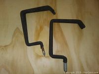 Two black metal screw-in L-shaped hooks on plywood surface