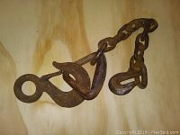Photo of a heavily rusted metal chain with large hook placed on plywood background.