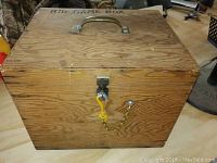 Closed view of the wooden game box showing the handle and lock with chain on the front panel.