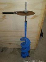 Manual ice auger with blue spiral blade and black grip handle against wooden background