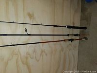 Photo shows three assorted fishing poles laying side by side on a wooden surface, highlighting different handle styles and rod lengths.