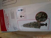 Box with branding and product information for the 4.5 foot pre-lit Norwich snow Christmas tree with decorative stand showing close-up of snowy needles and overall product image.