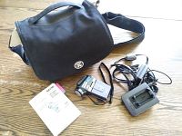 Camcorder alongside carrying case, charger, and instruction manual laid out on wood surface