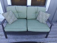Front view of outdoor love seat with green cushions and two chevron pillows