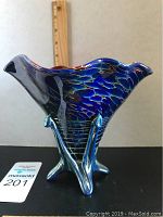 Side view of blue iridescent art glass vase on tripod glass base next to ruler for size reference.