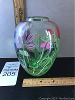 Front view of clear art glass vase with pink and purple floral encasement and green scrolling stems, showing scale with rulers.