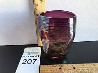 Side view of the purple glass vase with a wooden ruler for scale showing about 4 inches tall and a rounded, slightly asymmetrical shape with dark rim.