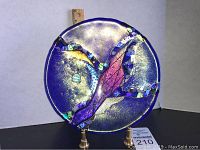 Front view of the signed art glass plate on a brass stand showing abstract design with purple and blue hues and iridescent textured details.