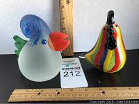 Front view of Borowski chick paper weight and colorful striped glass rooster with rulers showing size.