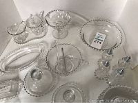 Photo showing assortment of Candlewick glass pieces on white backdrop including plates, bowls, trays, cruet set, and salt and pepper shakers, all with signature beaded edges.