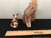 Three cat figurines placed on black background with rulers showing size. Larger orange tabby cat figurine with two smaller calico colored Goebel cats.