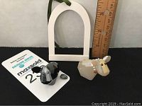 Two Swarovski crystal figurines on flat surface with ruler behind for size reference. Opal cow and black dog with detached ear visible.