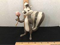 Full view of Lenox Pepe Le Pew figurine standing upright holding pink flower, with size ruler behind for scale.
