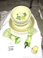 Photo showing stack of Franciscan Earthware dinnerware including plates and bowls with green and yellow floral pattern, alongside two green glass bird figurines and a small spiral-shaped glass perfume bottle with yellow stopper.