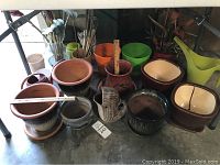 Photo showing nine garden pots of various sizes and two watering pitchers arranged on floor.