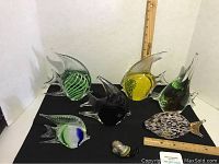 Seven glass fish art sculptures displayed on black fabric with measuring ruler for scale.