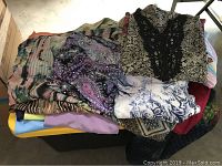 Photo showing a assorted pile of ladies tops in various patterns and colors including paisley, floral, and solid colors.