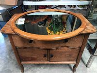 Front view of the wooden cabinet with oval mirror placed on top.