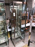 Full view of tall glass display case with metal framing, glass door, and multiple glass shelves inside. Shelves are packed separately and not installed.